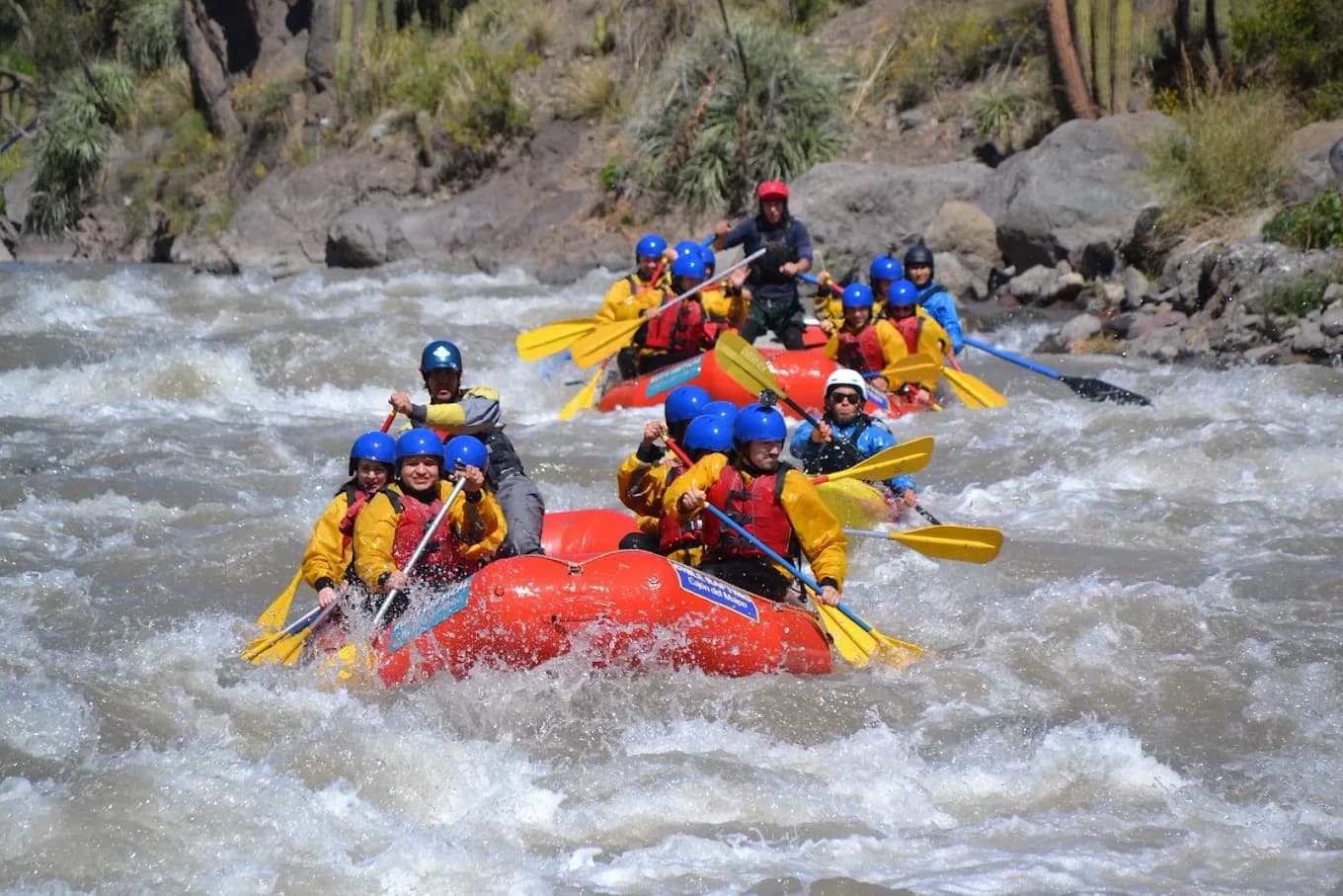 Dois botes de rafting descendo um rápido de água cinza em um cânion de montanha seca