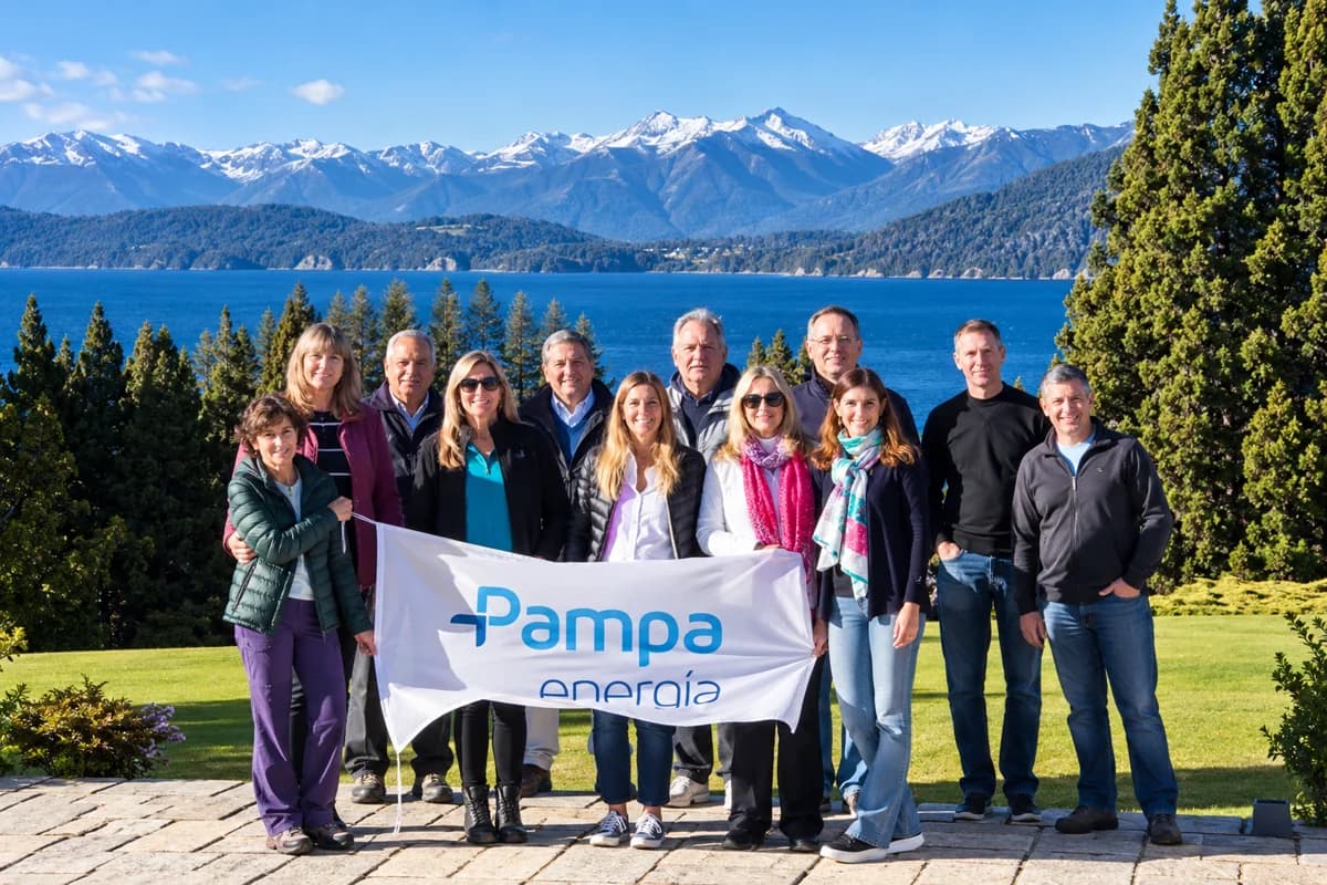 Grupo de uma empresa posando com sua bandeira em frente ao lago e à cordilheira nevada