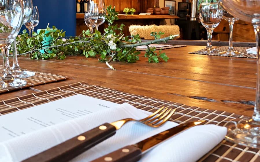 Mesa montada para um jantar de empresa numa cabana de madeira, com taças e ramos naturais