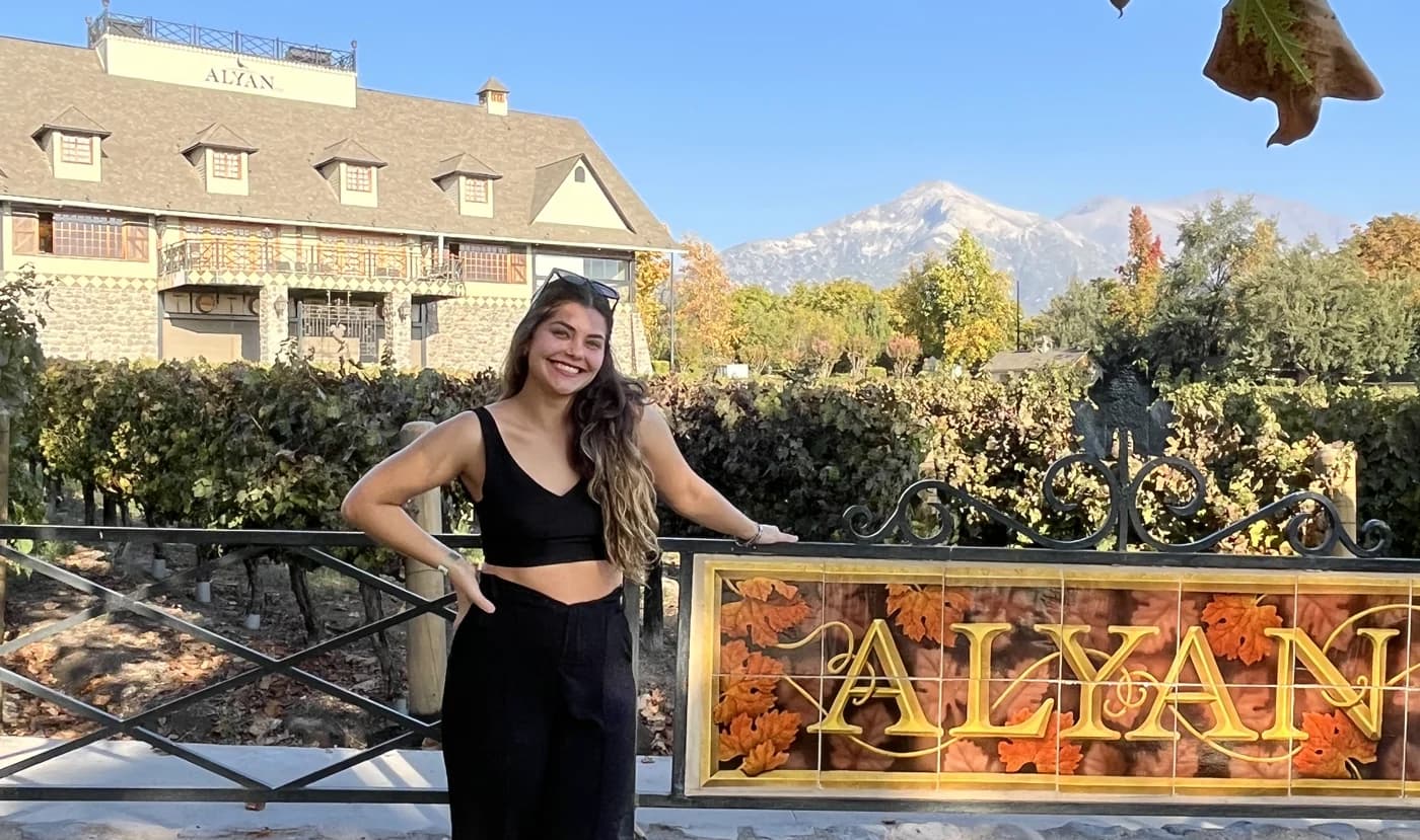 Vines and the Alyan winery sign, with the winery building and the mountains behind in the late afternoon