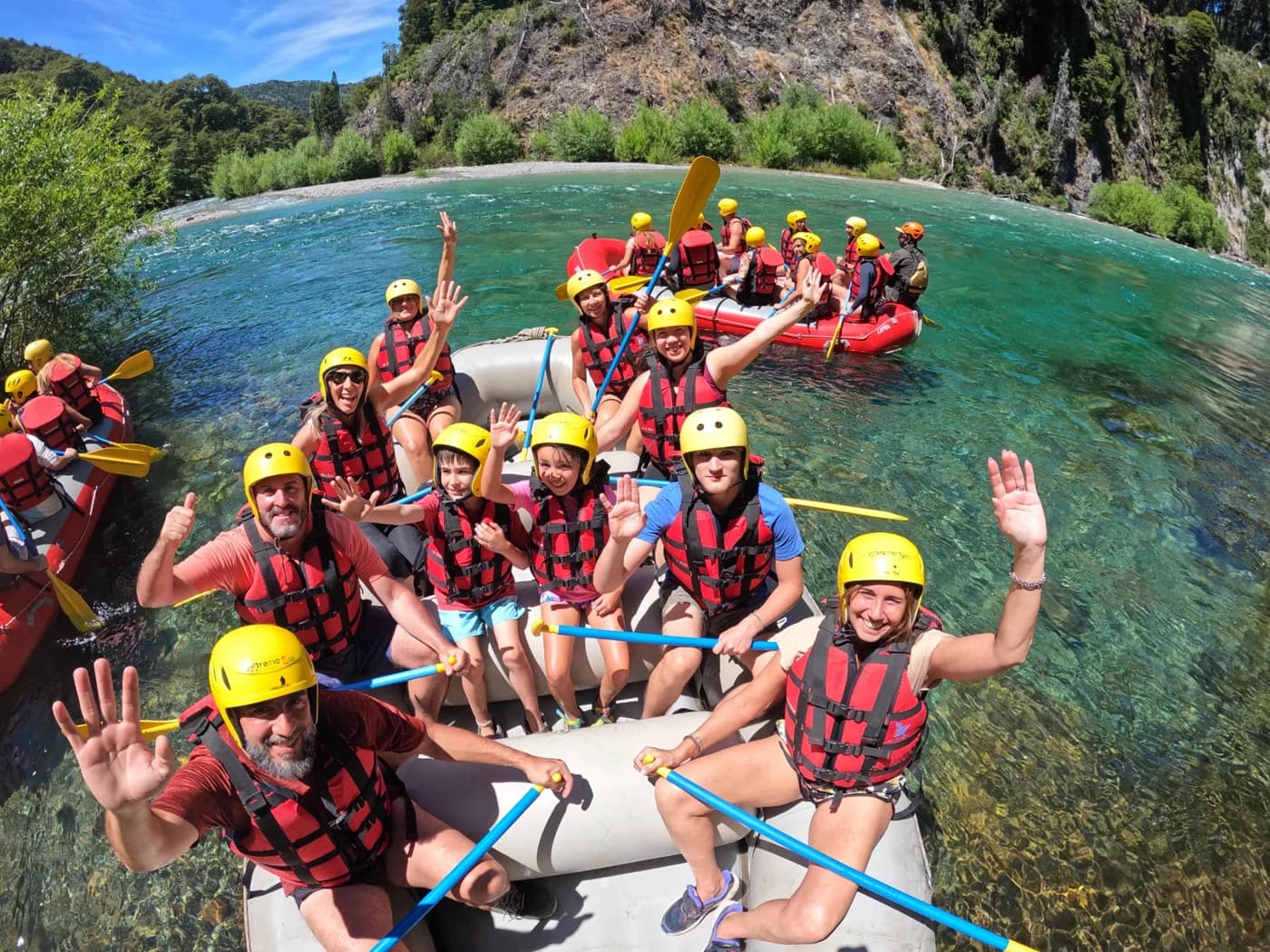 A rafting group in helmets and life jackets on turquoise water, between forest and rock walls