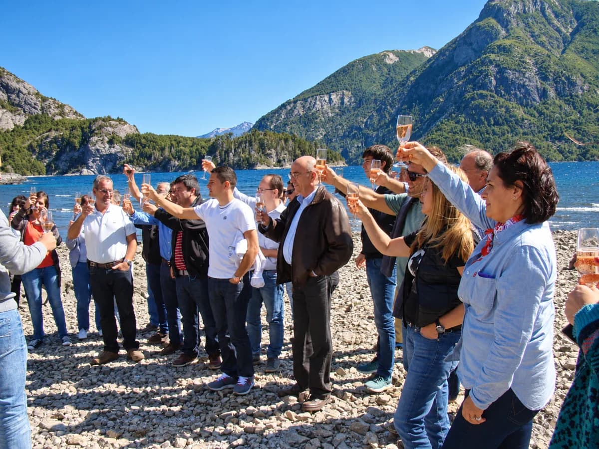 Grupo de uma empresa brindando com taças levantadas à beira do lago, com as montanhas atrás