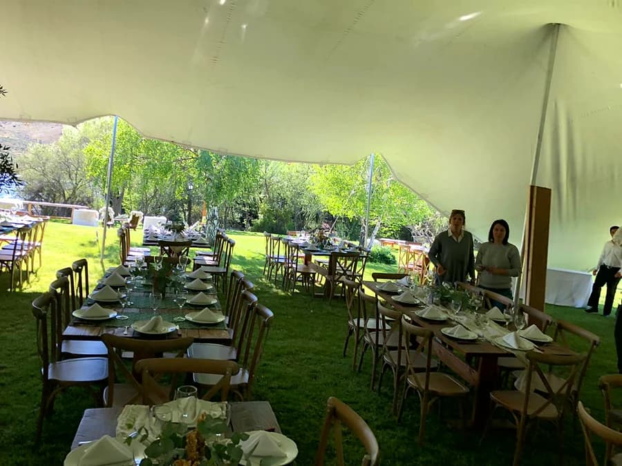 Interior de la carpa con mesas servidas y el parque de fondo