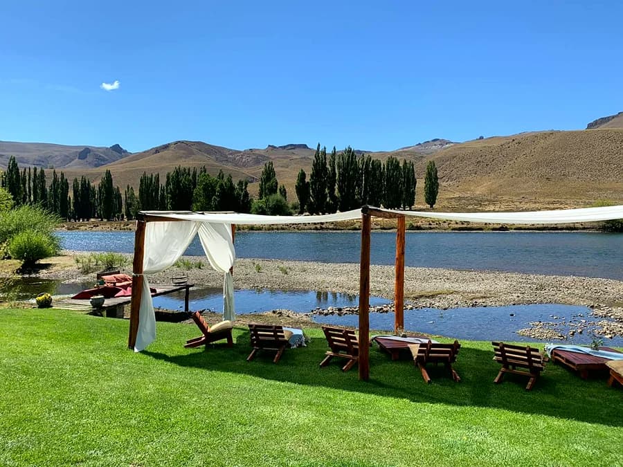 Pérgola con telas blancas y reposeras a la orilla del río