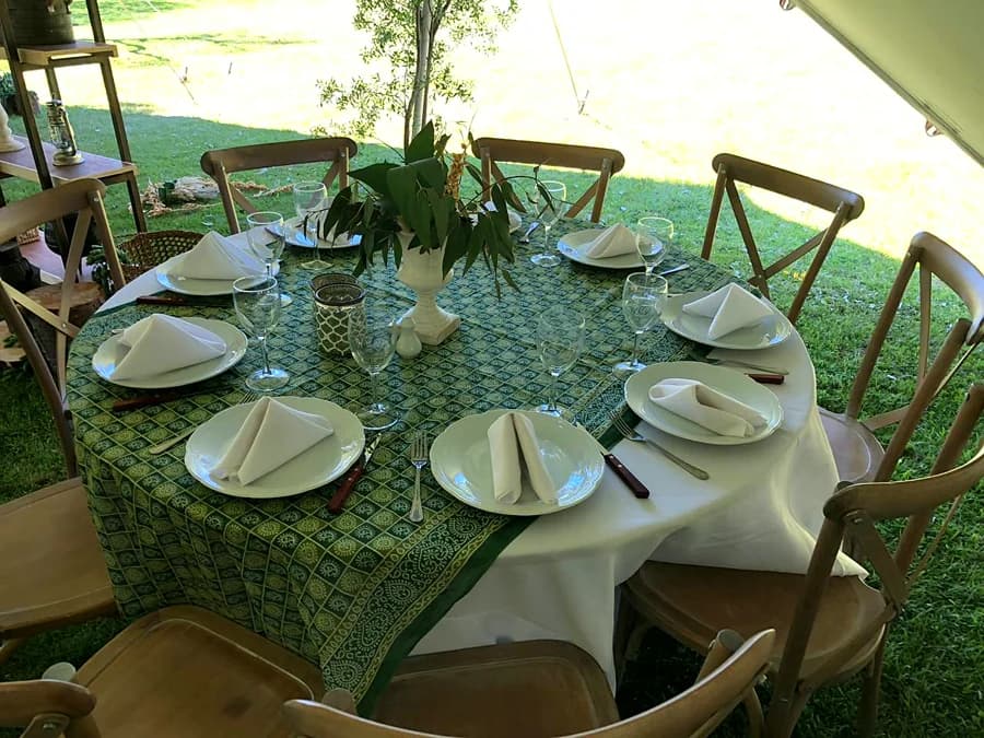 Mesa redonda montada con mantelería, vajilla y copas, bajo la carpa